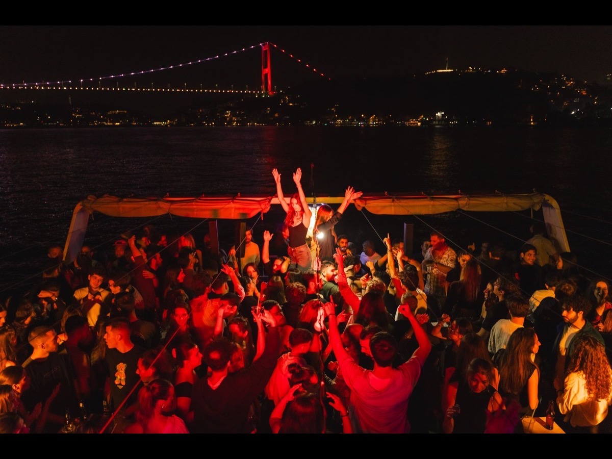Party boat sailing past the Bosphorus Bridge lit up red at night