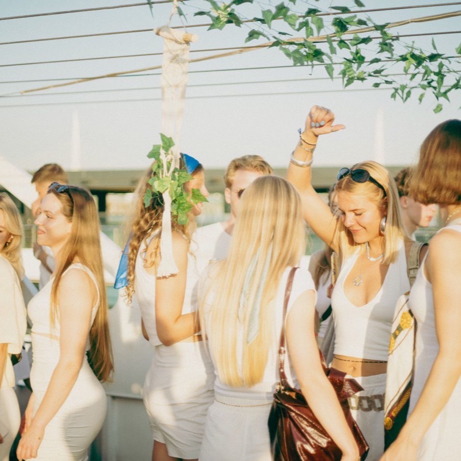 Guests in the all-white dress code dancing on deck at golden hour
