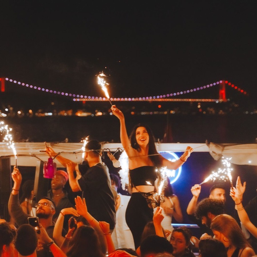 Guest holding a sparkler on deck with the Bosphorus Bridge lit up at night