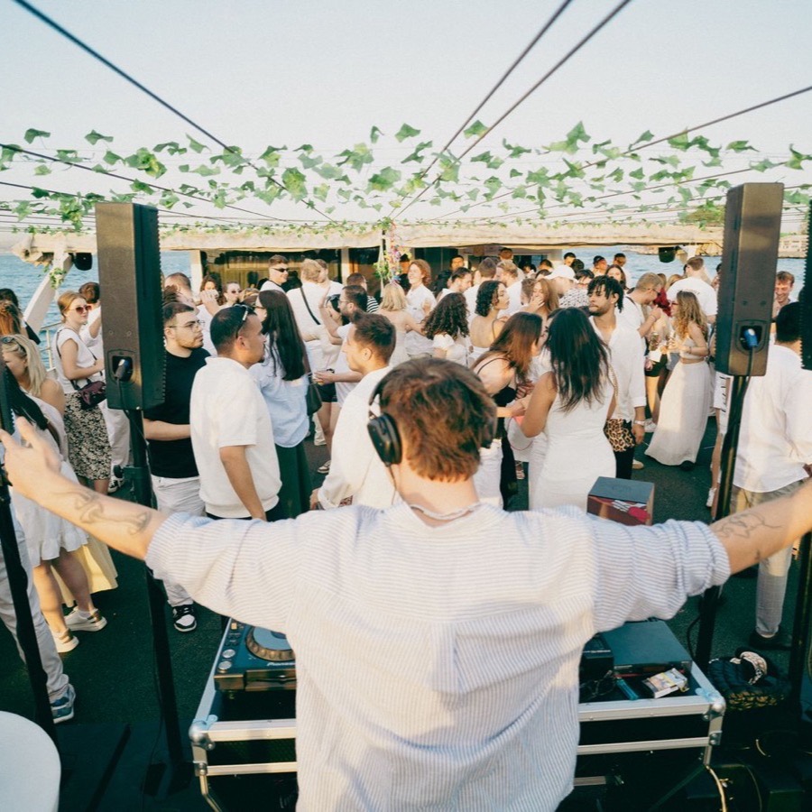 DJ performing on deck for a crowd in white at golden hour