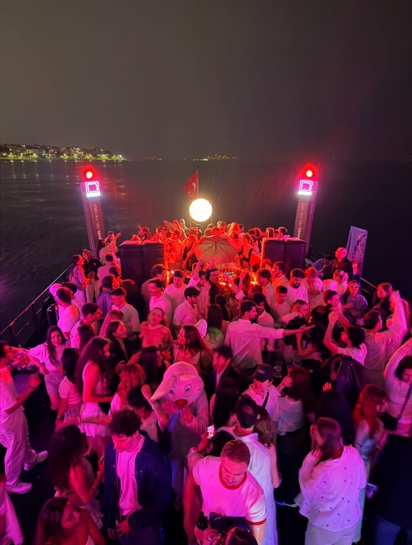 Guests dancing on deck at night under red and pink party lights